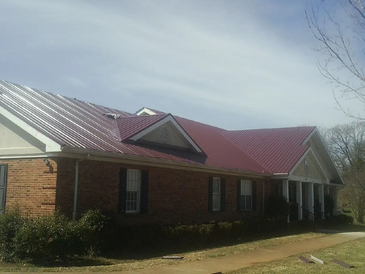Red metal roof with gabled entries on a long brick building, from a Hail Damage Roof Repair job in Valley Head