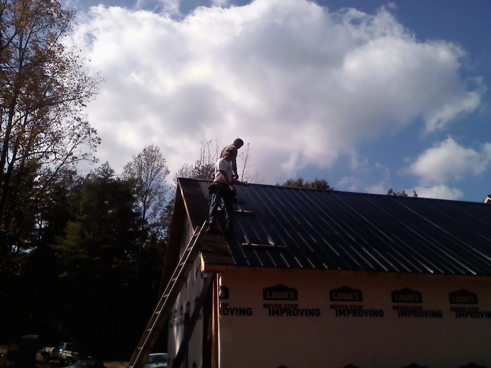 Roofer fastening dark metal panels high against a cloudy sky, from a Roof Inspection job in Valley Head