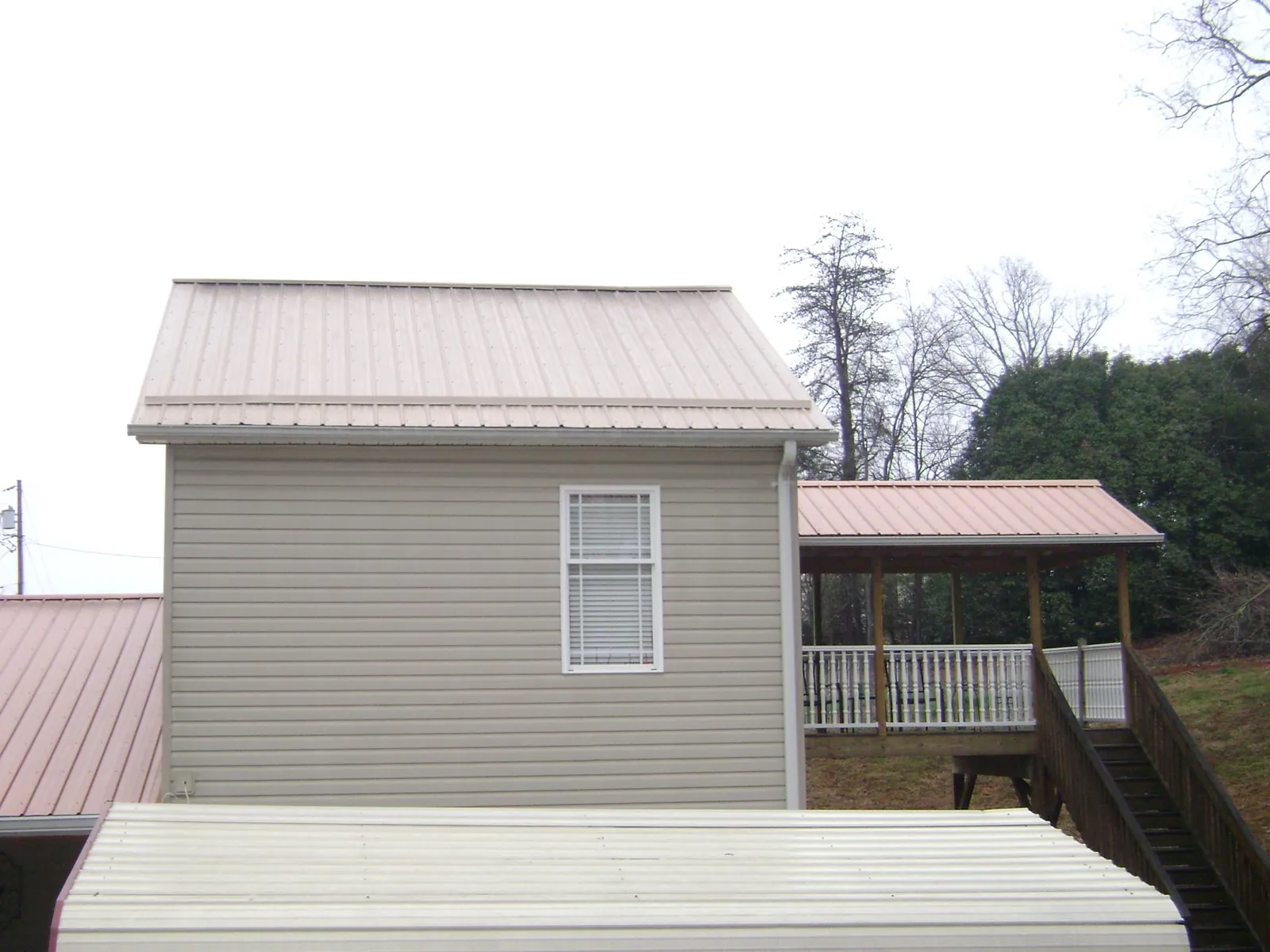 Tan metal roofs on a two story addition and attached porch, from a Roof Replacement job in Valley Head